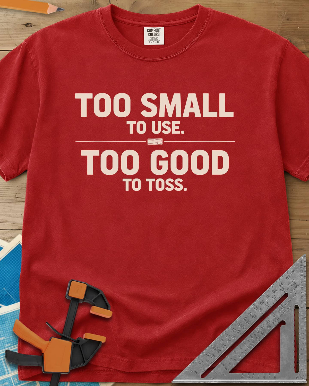 Too Small To Use Too Good To Toss heavyweight tee in Red, two-line slogan split by a rule with a tiny wood offcut