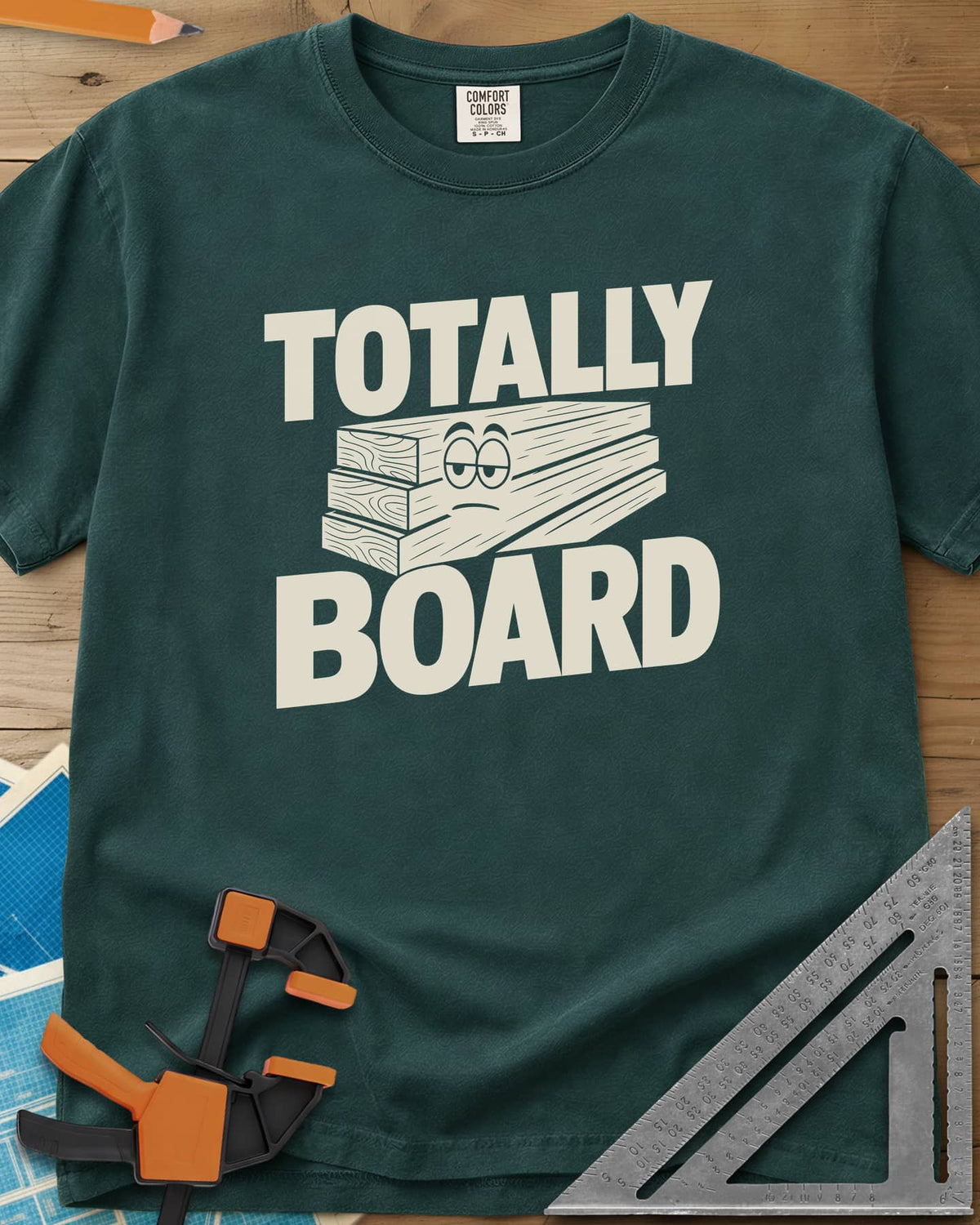 Totally Board heavyweight tee in Blue Spruce, a stack of three planks wearing a bored, half-lidded face