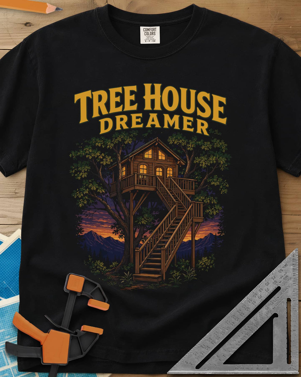 Tree House Dreamer heavyweight tee in Black, a glowing wooden treehouse with a long staircase at sunset