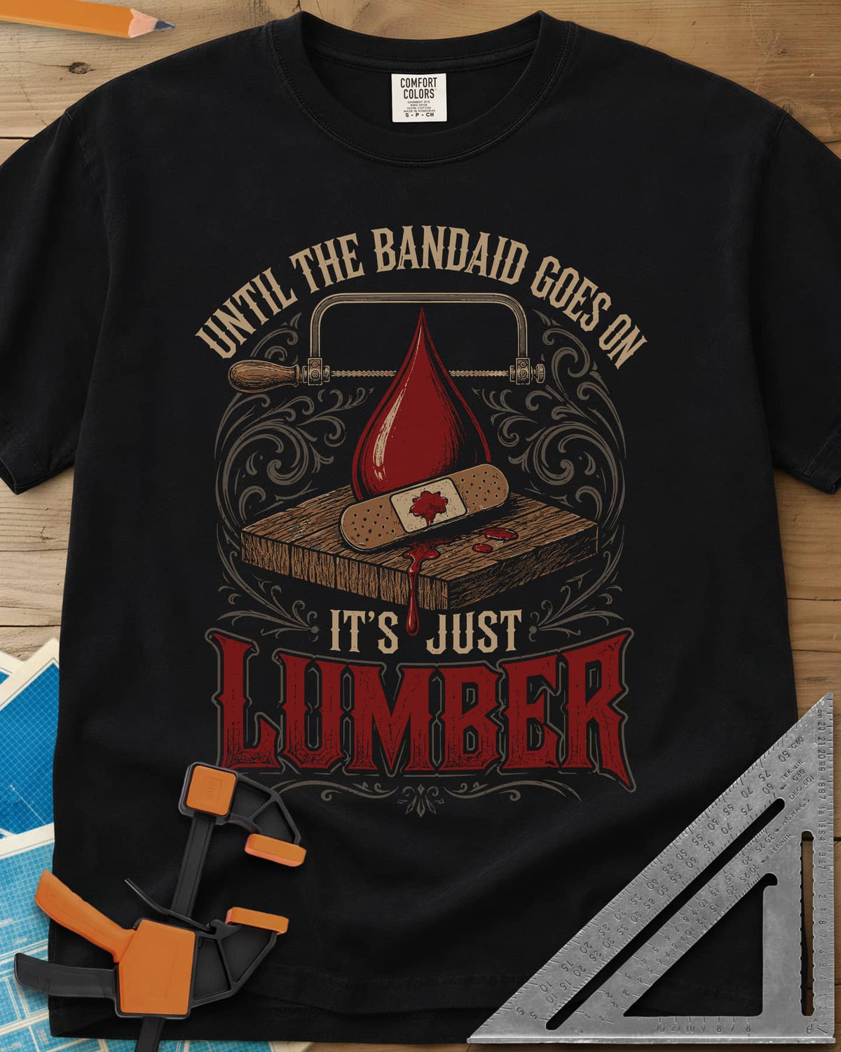 Until The Bandaid Goes On It's Just Lumber heavyweight tee in Black, frame saw, red drop and a bandaid on a board with