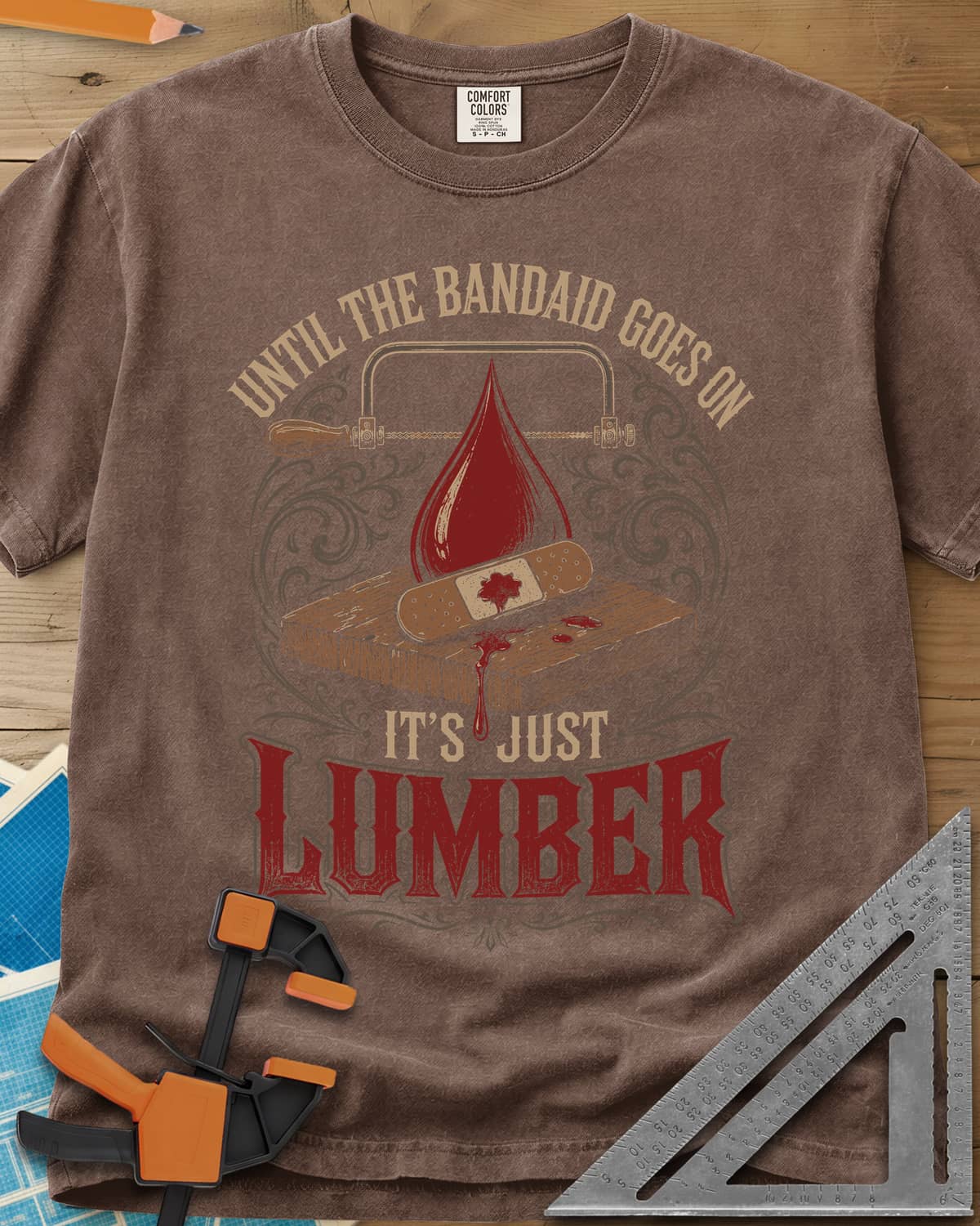 Until The Bandaid Goes On It's Just Lumber heavyweight tee in Espresso, frame saw, red drop and a bandaid on a board with