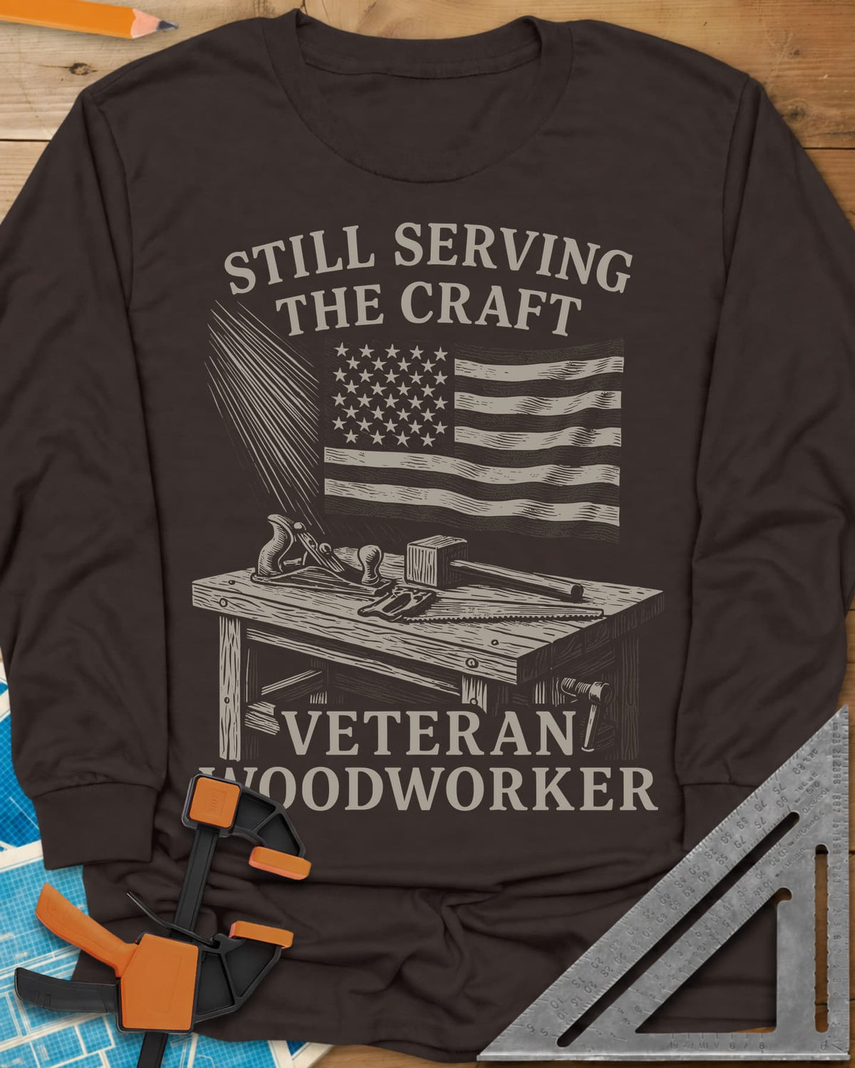Veteran Woodworker long sleeve shirt in Dark Chocolate, an American flag over a workbench with a plane, mallet and saw