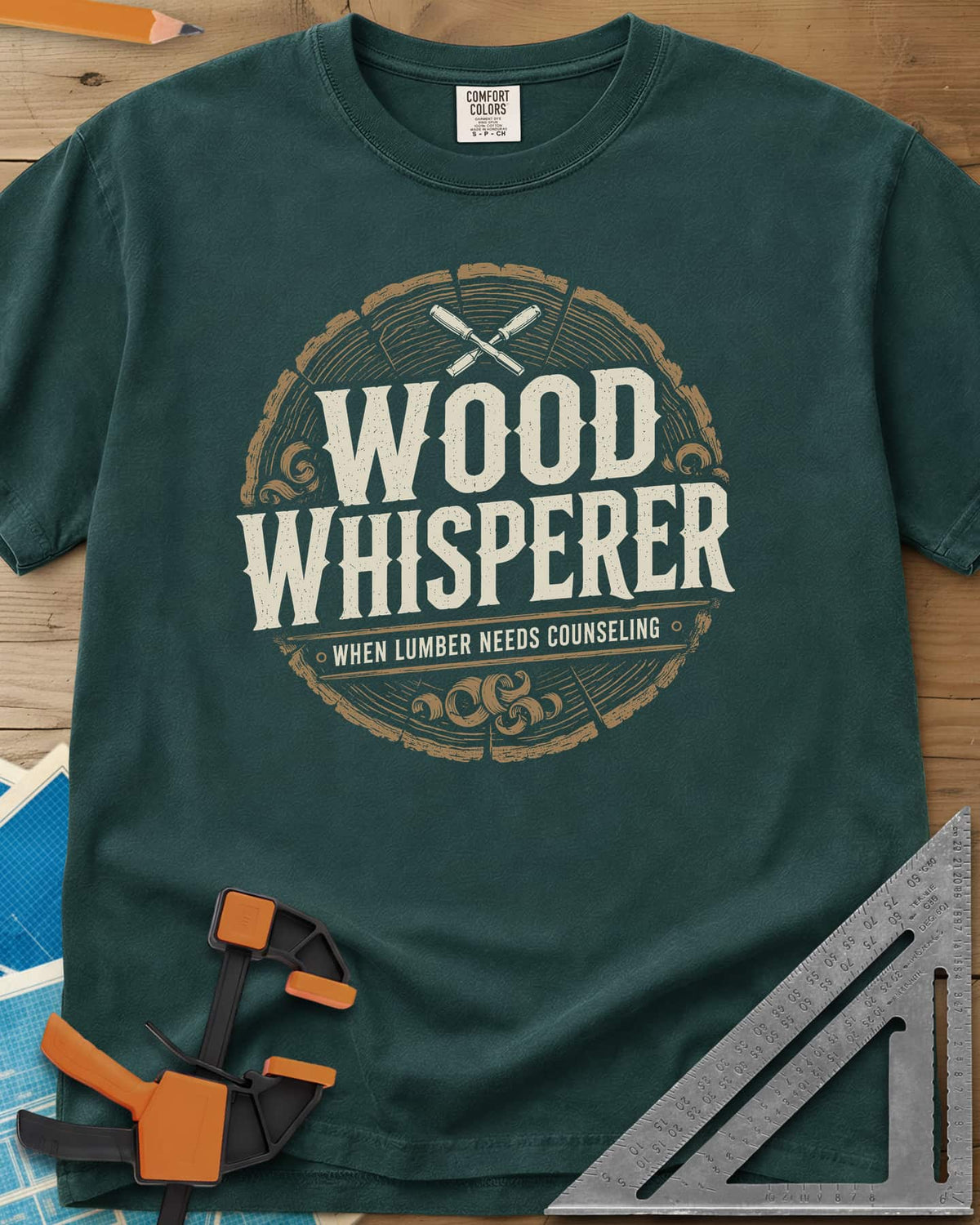 Wood Whisperer heavyweight tee in Blue Spruce, a round log-slice badge with crossed chisels and shaving curls