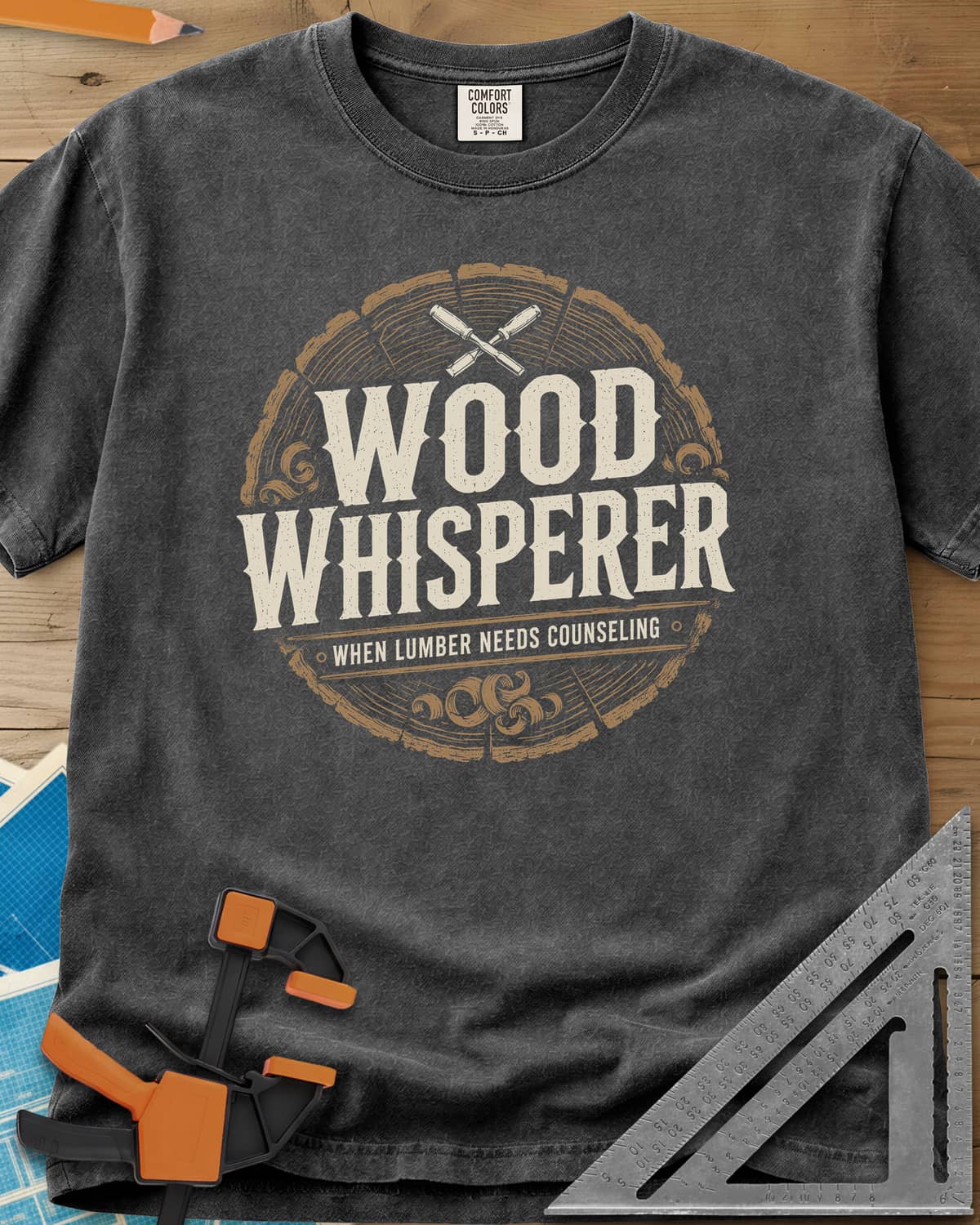 Wood Whisperer heavyweight tee in Pepper, a round log-slice badge with crossed chisels and shaving curls