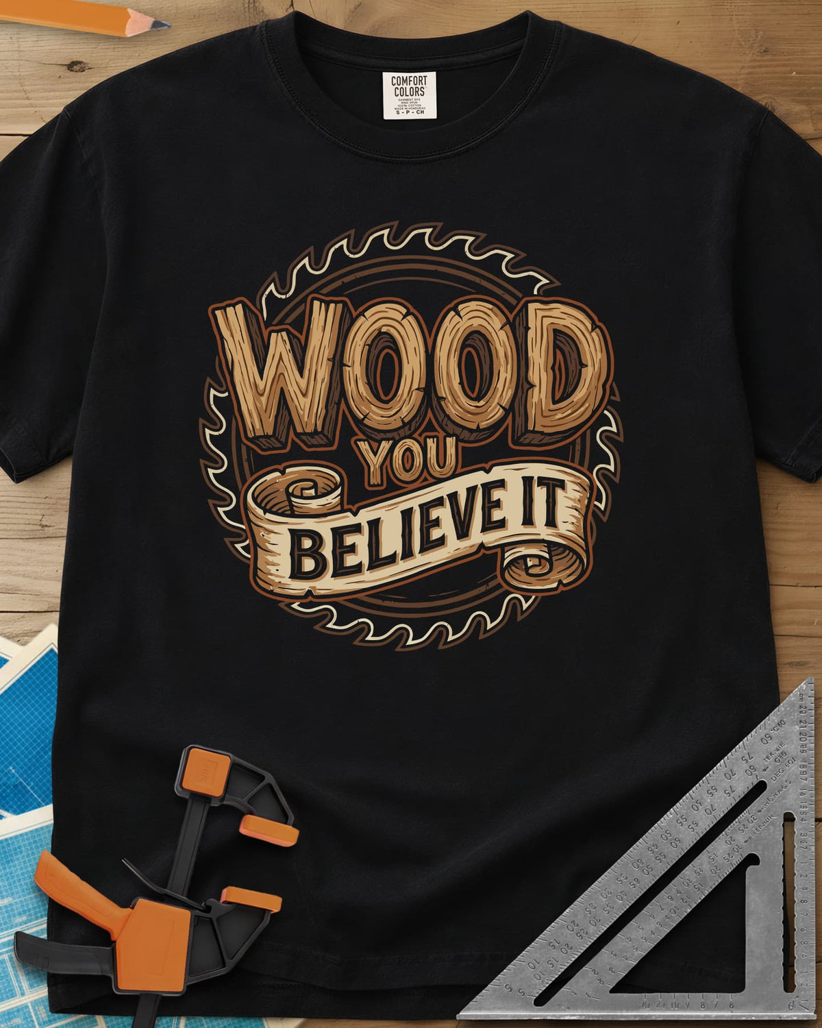 Wood You Believe heavyweight tee in Black, wood-grain letters on a scroll banner over a circular saw blade
