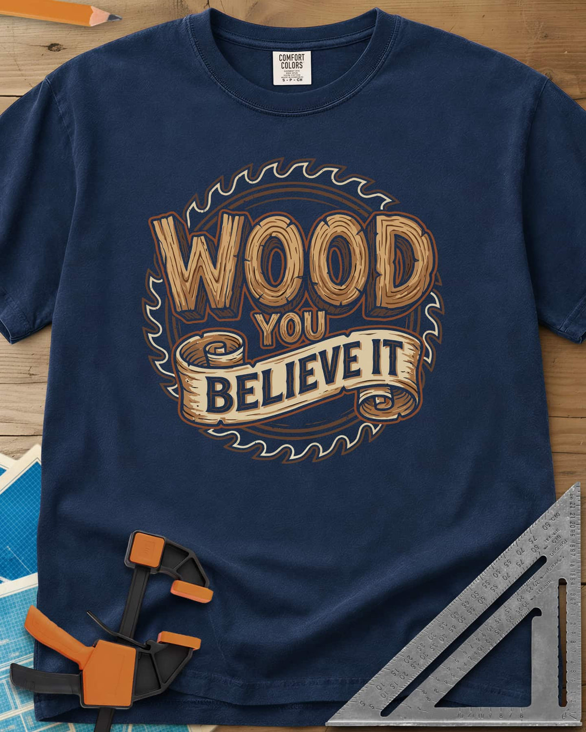 Wood You Believe heavyweight tee in Navy, wood-grain letters on a scroll banner over a circular saw blade