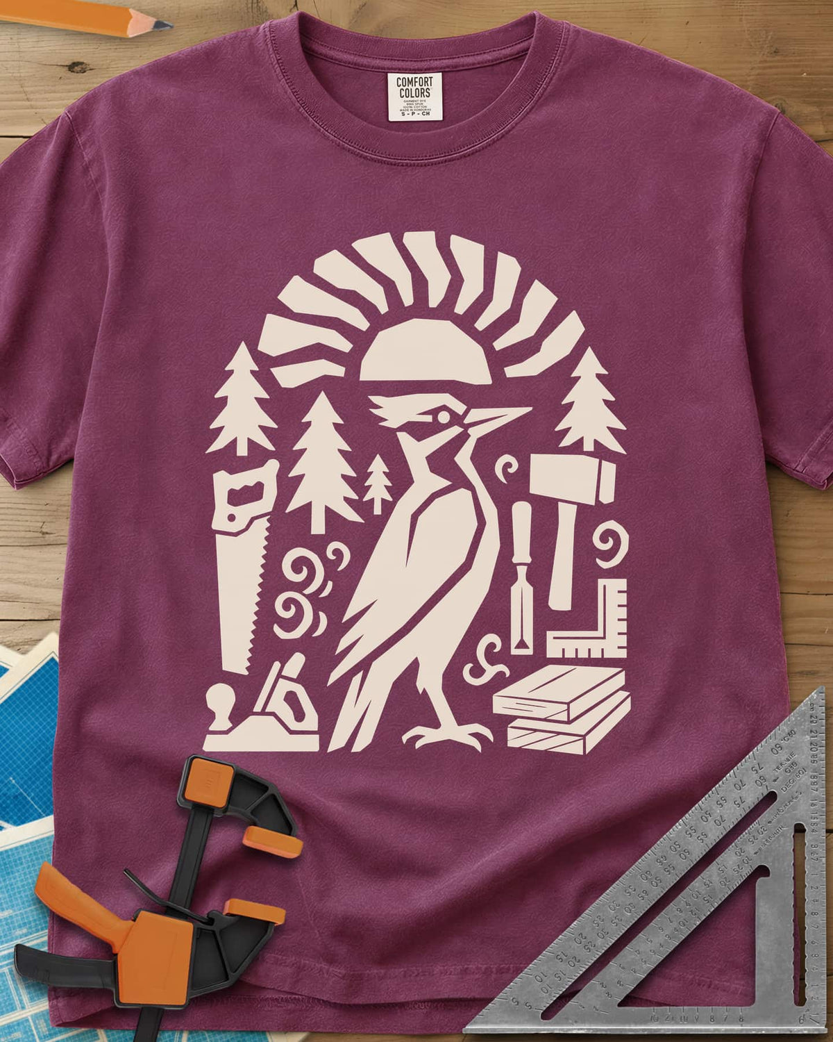 Woodpecker Craft heavyweight tee in Berry, a geometric woodpecker among saws, planes, chisels and pine trees