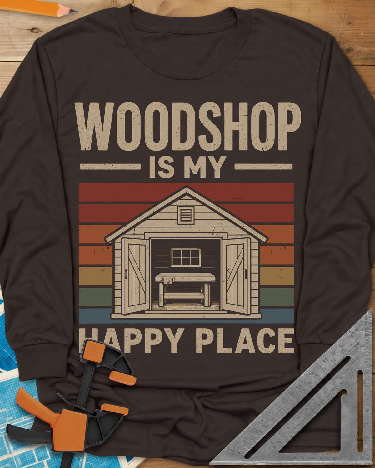 Woodshop Happy Place long sleeve shirt in Dark Chocolate, a small shed with open doors and a workbench on retro sunset