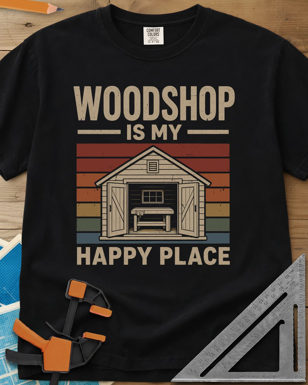 Woodshop Happy Place heavyweight tee in Black, a small shed with open doors and a workbench on retro sunset stripes