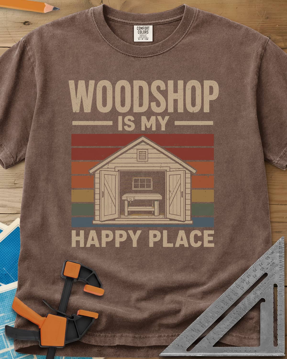 Woodshop Happy Place heavyweight tee in Espresso, a small shed with open doors and a workbench on retro sunset stripes