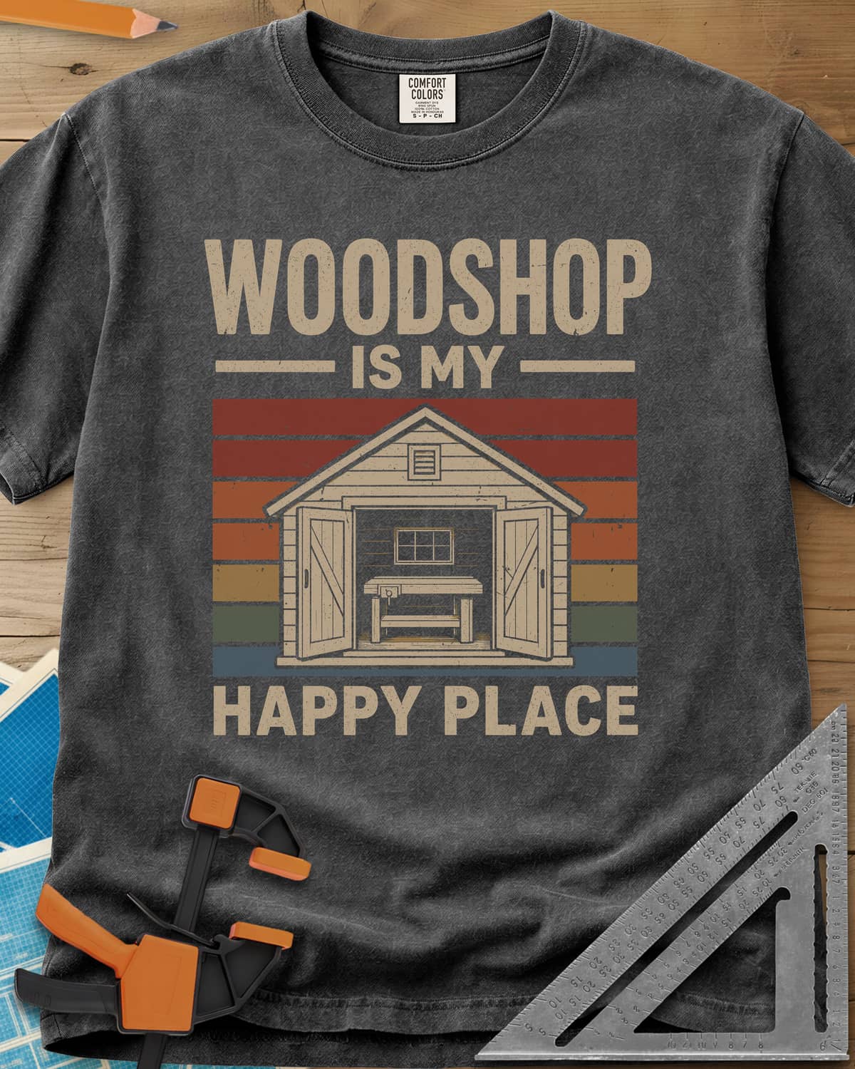 Woodshop Happy Place heavyweight tee in Pepper, a small shed with open doors and a workbench on retro sunset stripes