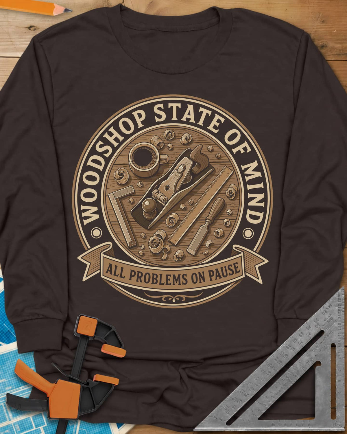 Woodshop State Of Mind long sleeve shirt in Dark Chocolate, a round badge of a hand plane, coffee, chisel and shavings on a