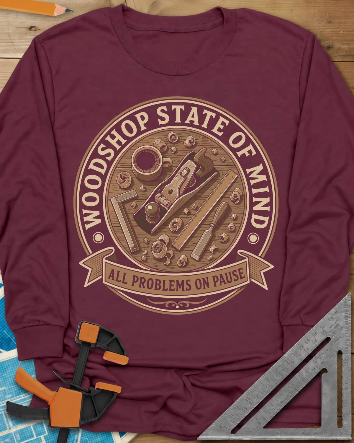 Woodshop State Of Mind long sleeve shirt in Maroon, a round badge of a hand plane, coffee, chisel and shavings on a bench
