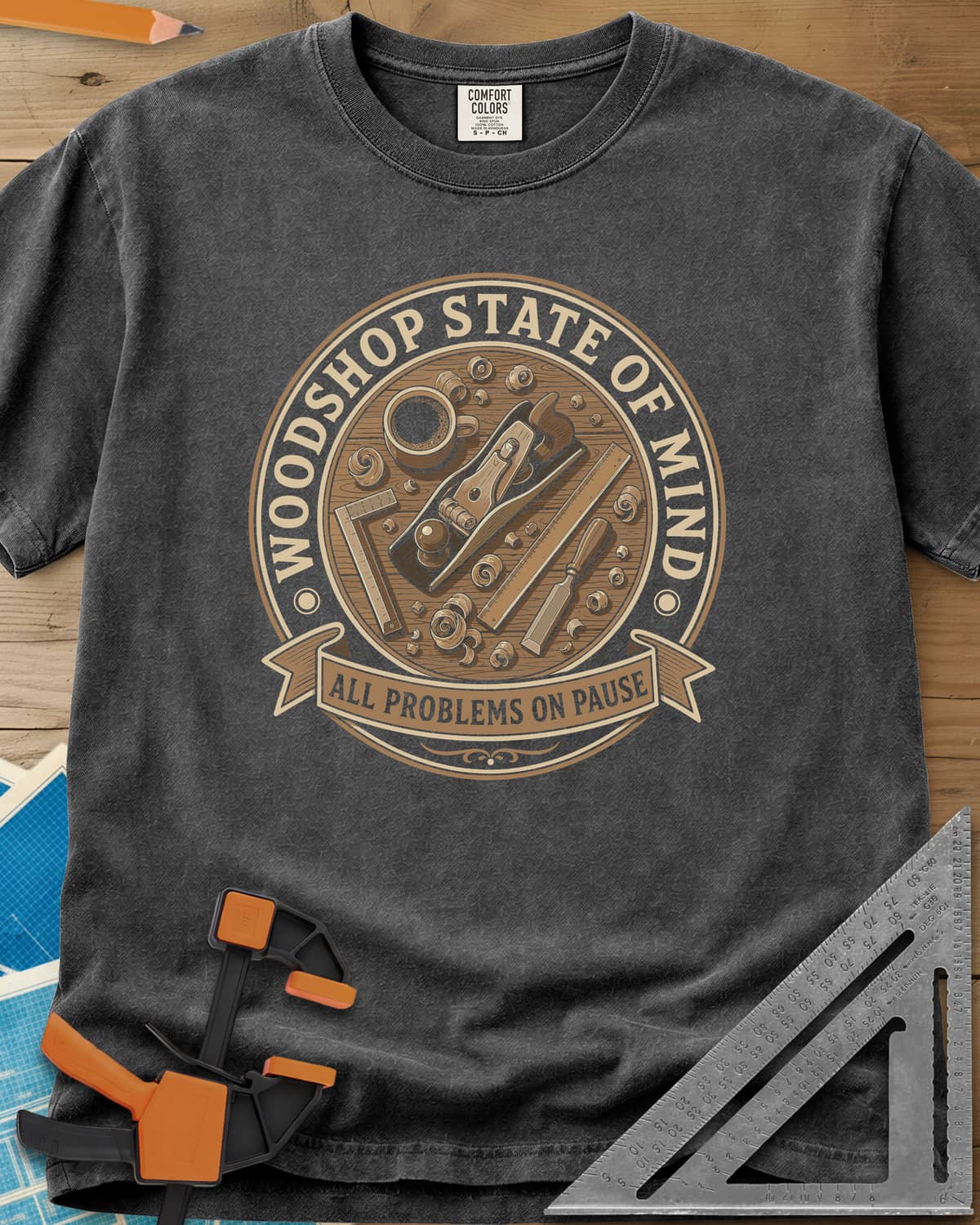 Woodshop State Of Mind heavyweight tee in Pepper, a round badge of a hand plane, coffee, chisel and shavings on a bench