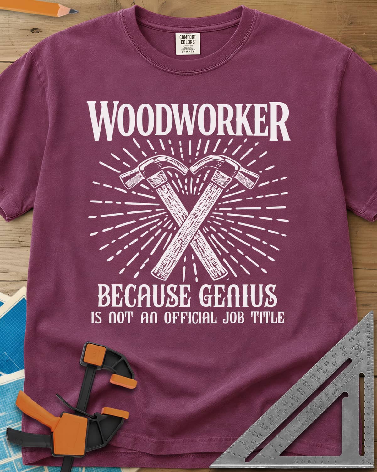 Woodworker Because Genius heavyweight tee in Berry, two crossed hammers inside a sunburst of fine lines
