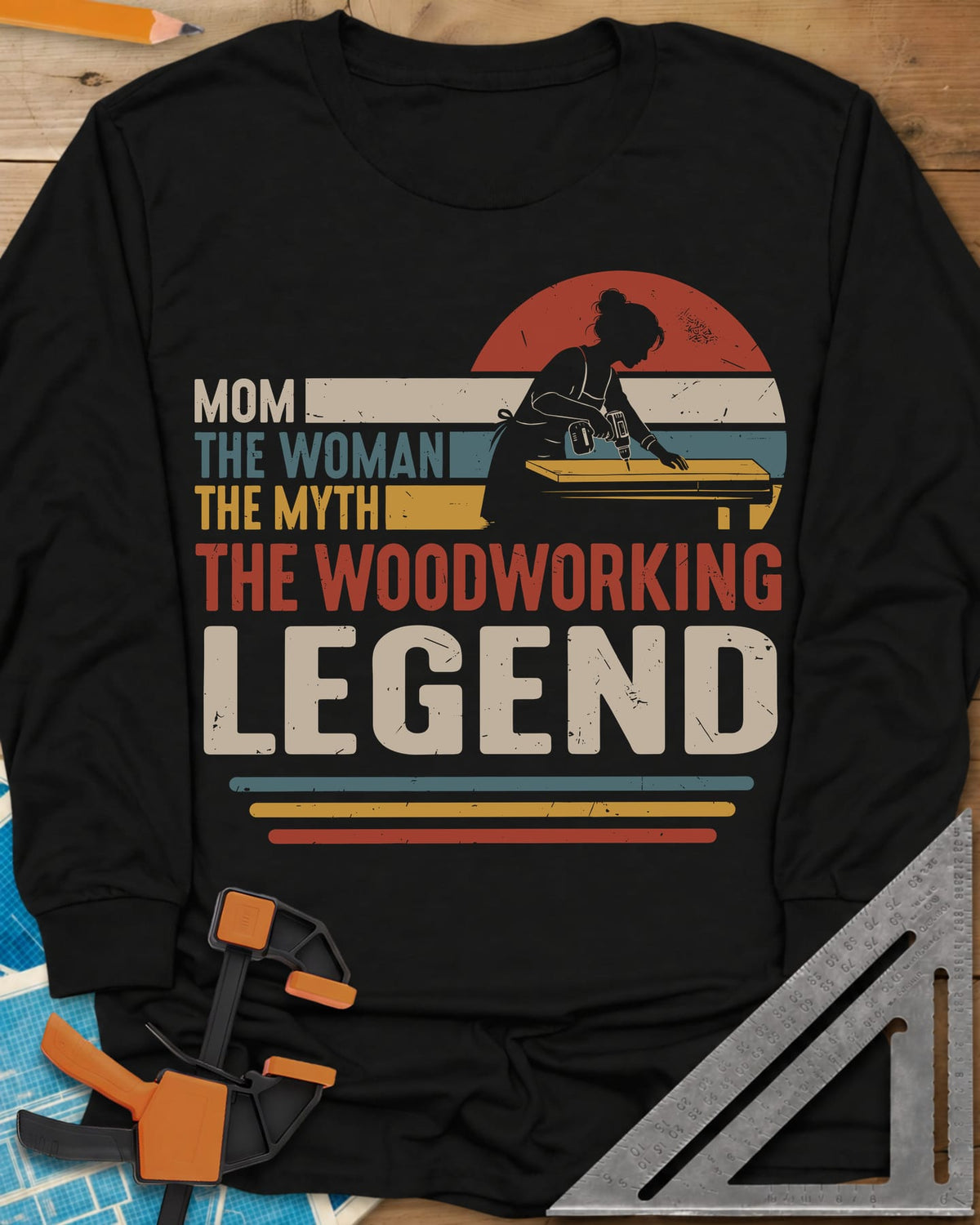 Woodworking Mom Legend long sleeve shirt in Black, a woman drilling into a board in front of a retro sunset