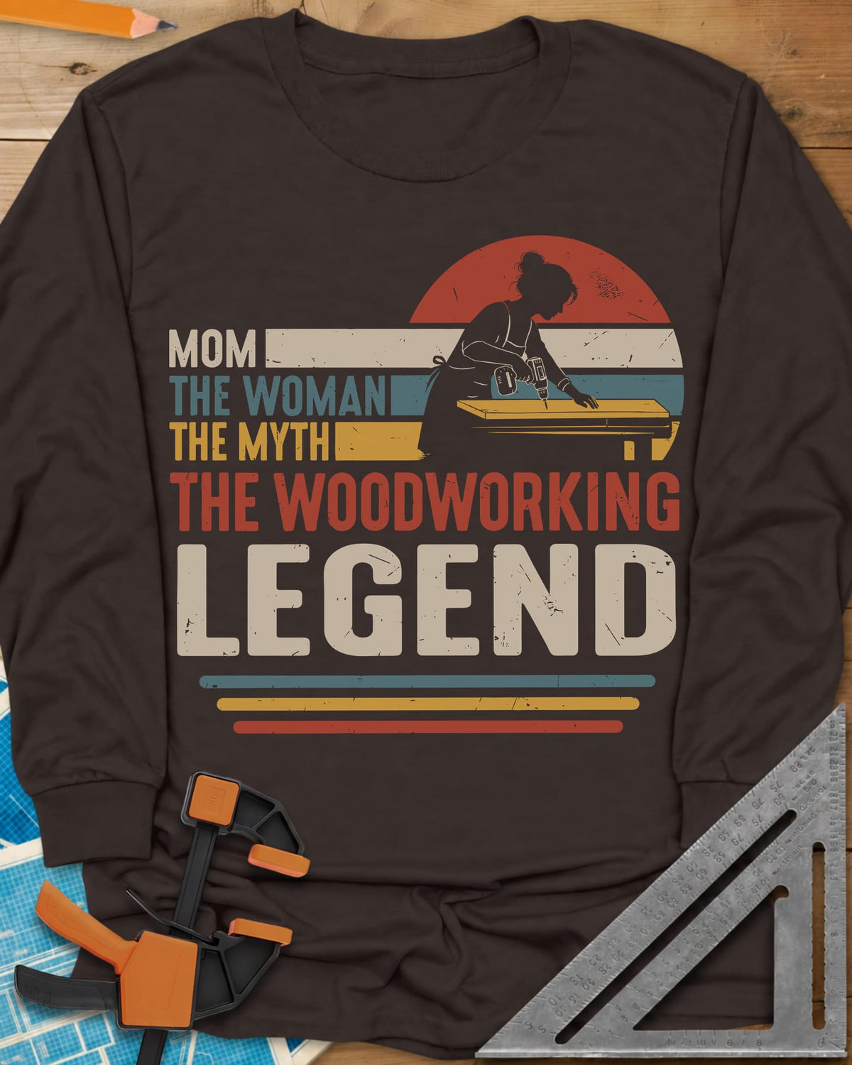 Woodworking Mom Legend long sleeve shirt in Dark Chocolate, a woman drilling into a board in front of a retro sunset