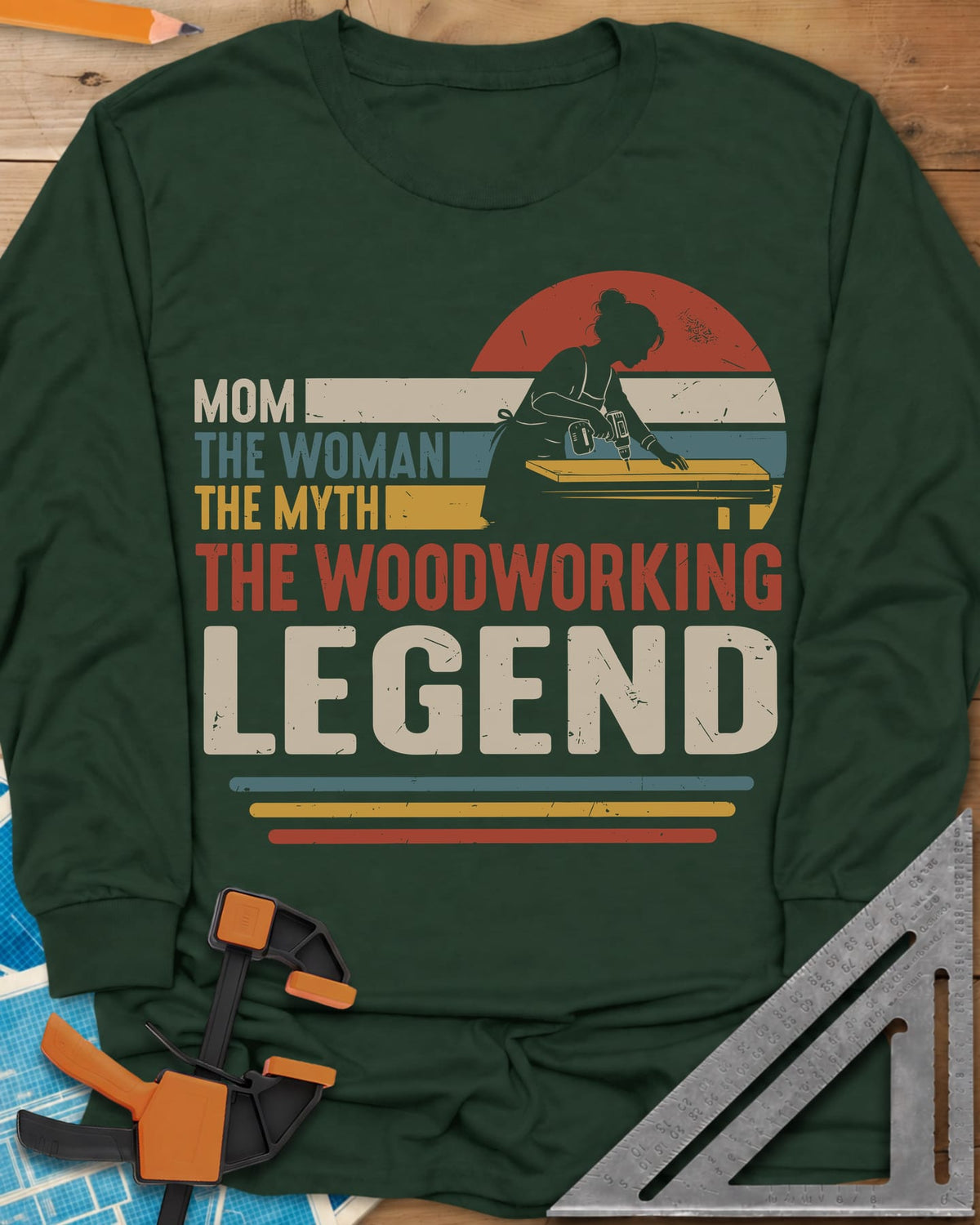 Woodworking Mom Legend long sleeve shirt in Forest Green, a woman drilling into a board in front of a retro sunset