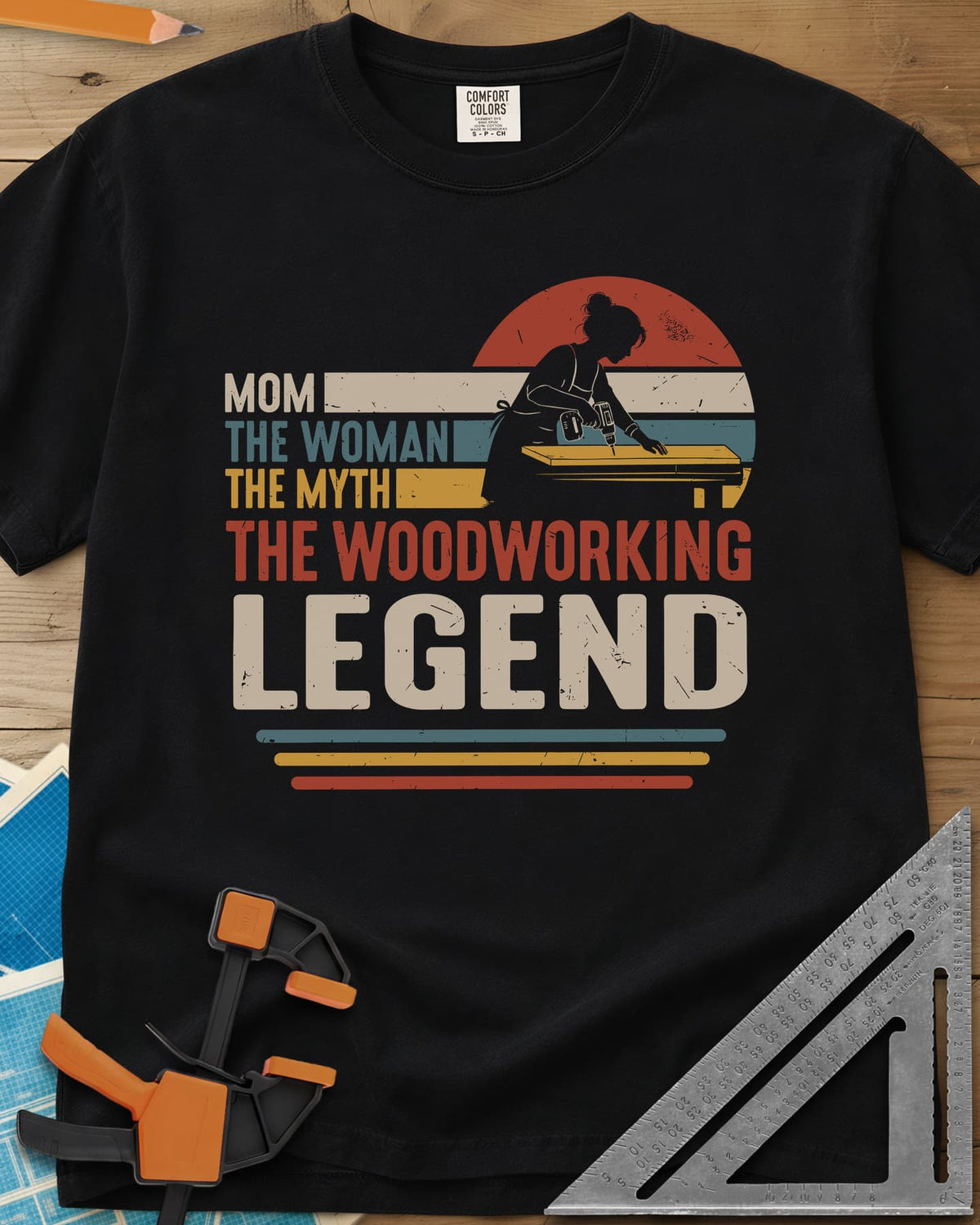 Woodworking Mom Legend heavyweight tee in Black, a woman drilling into a board in front of a retro sunset