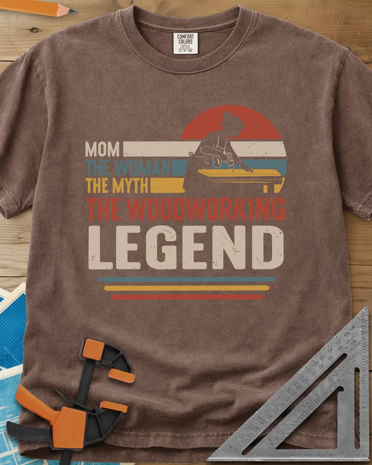 Woodworking Mom Legend heavyweight tee in Espresso, a woman drilling into a board in front of a retro sunset