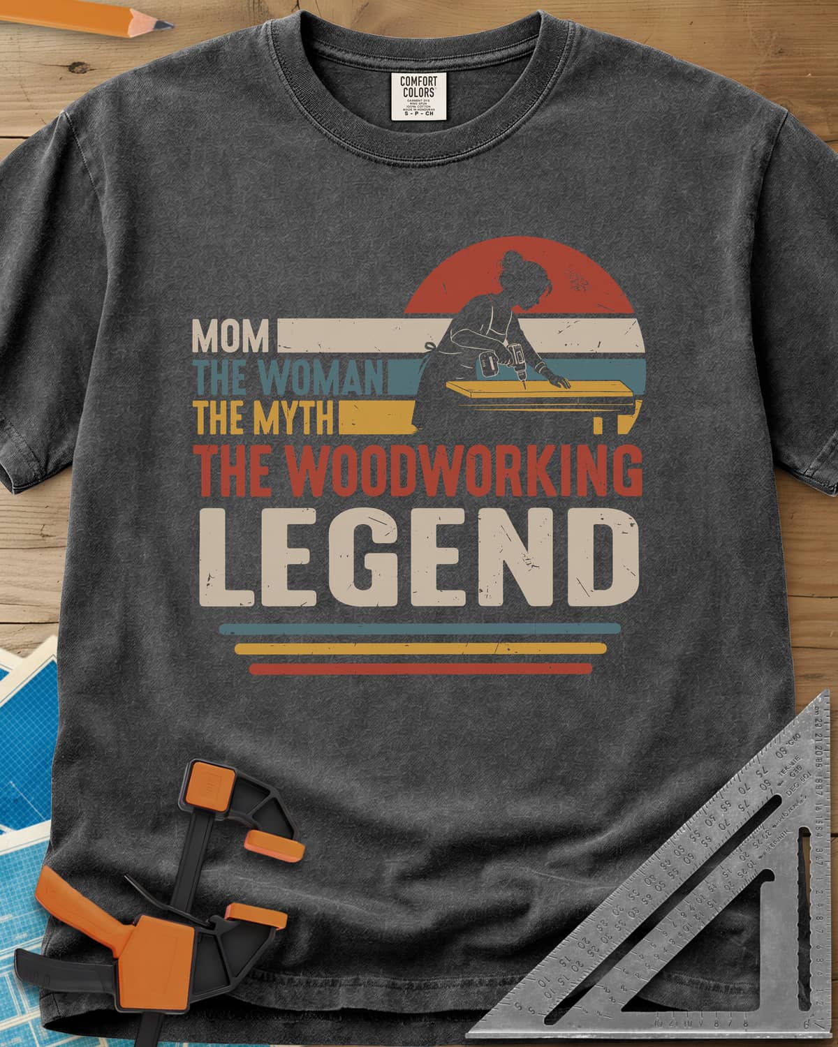 Woodworking Mom Legend heavyweight tee in Pepper, a woman drilling into a board in front of a retro sunset